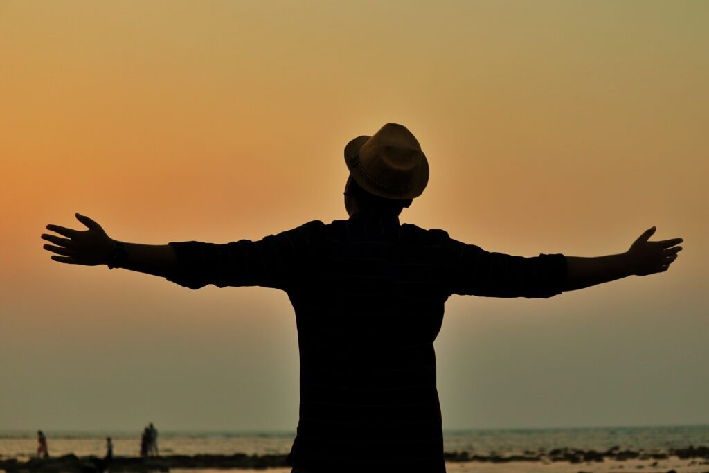 A person in silhouette, wearing a fedora, spreads arms at sunset on a beach in Saint Martin.